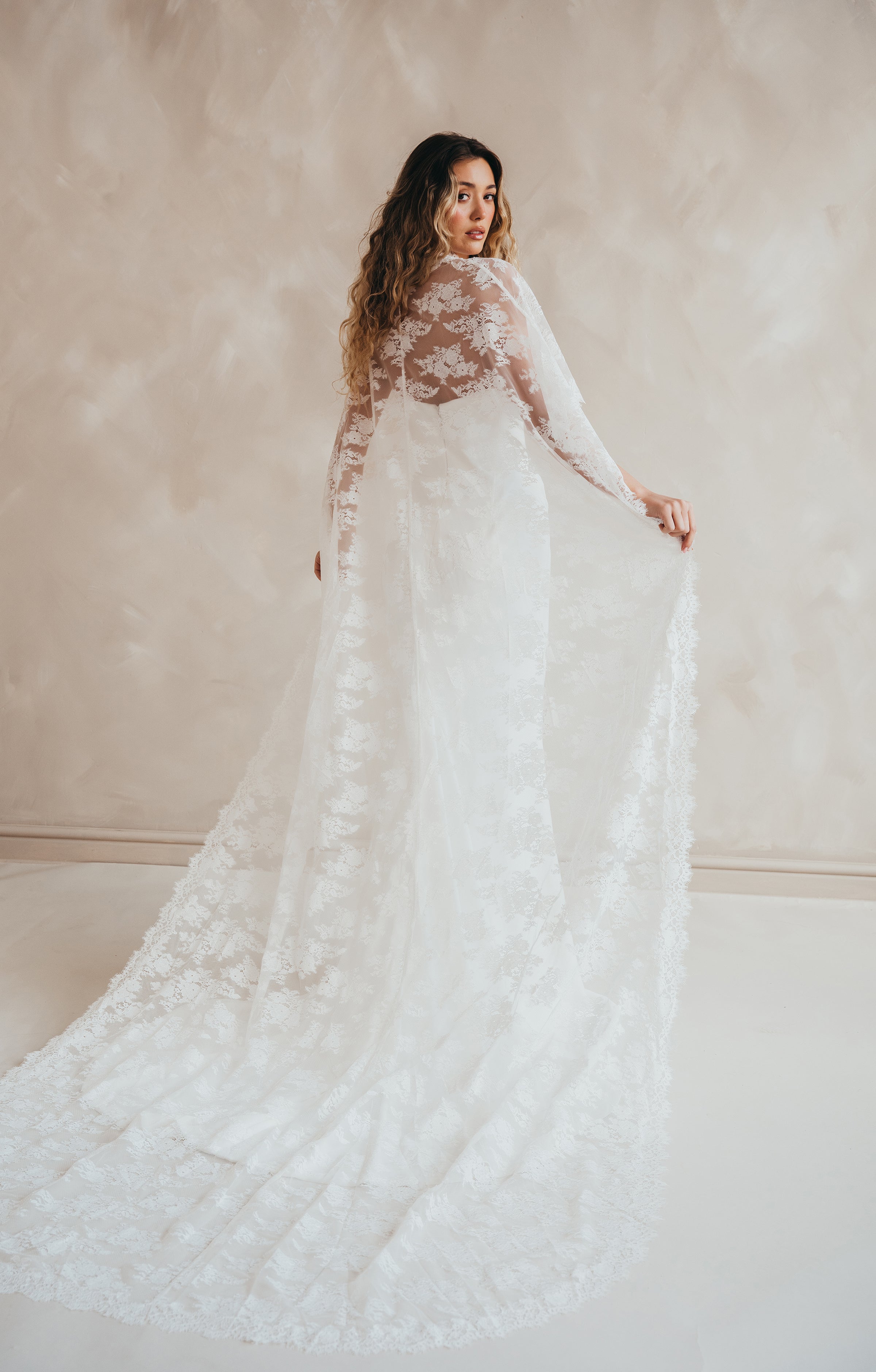 Bride wearing the Lace Roxie bridal cape with high neckline and intricate lace detail.