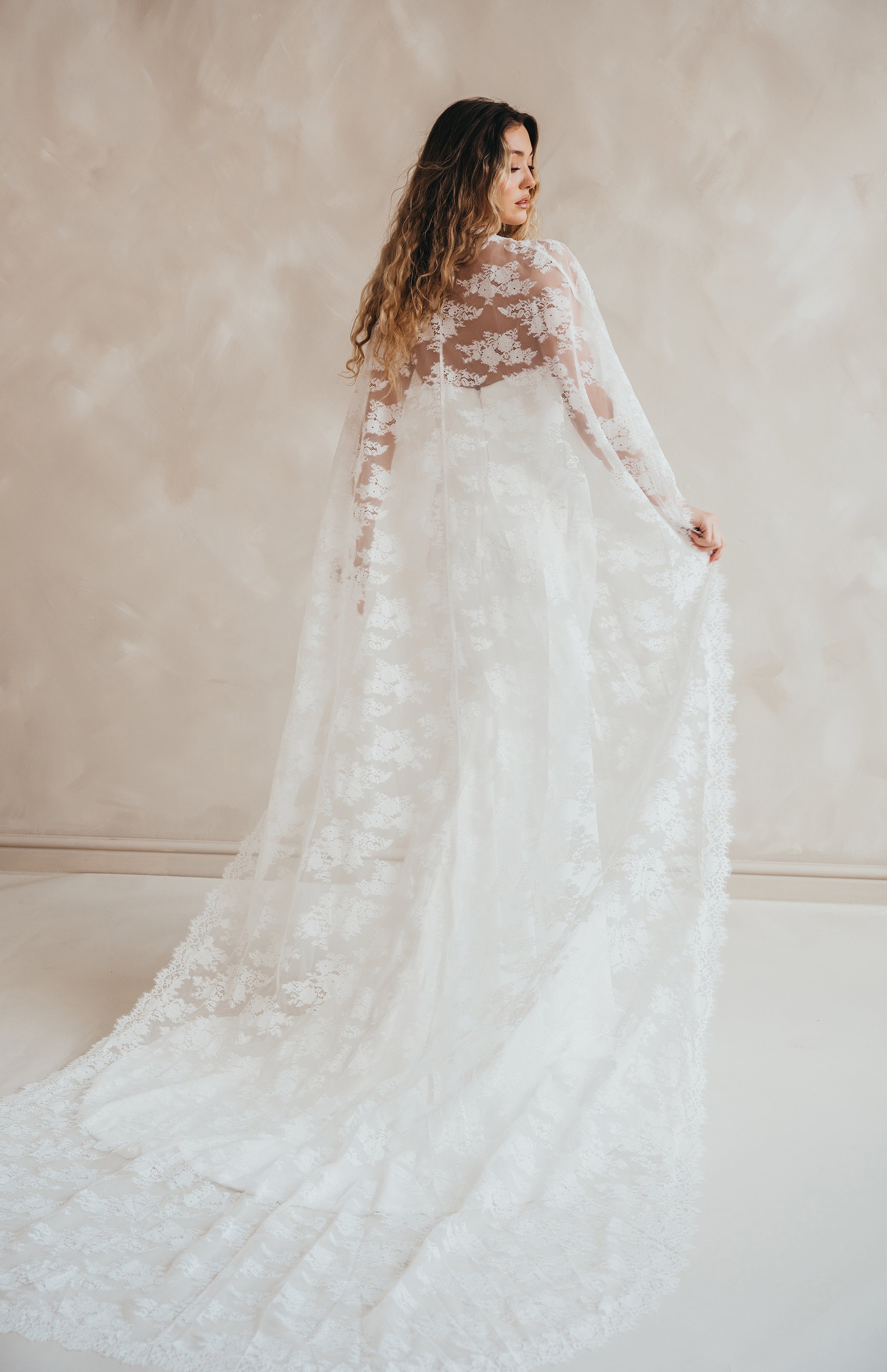 Bride wearing the Lace Roxie bridal cape with high neckline and intricate lace detail.
