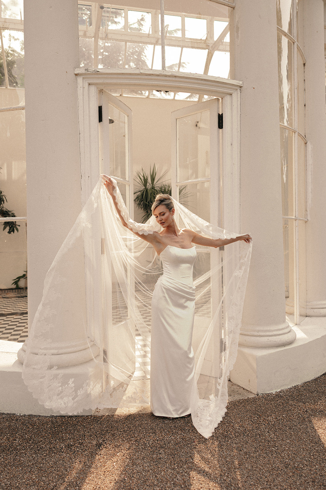 Woman in a ivory wedding dress with a long lace wedding veil in a bright, sunlit room.