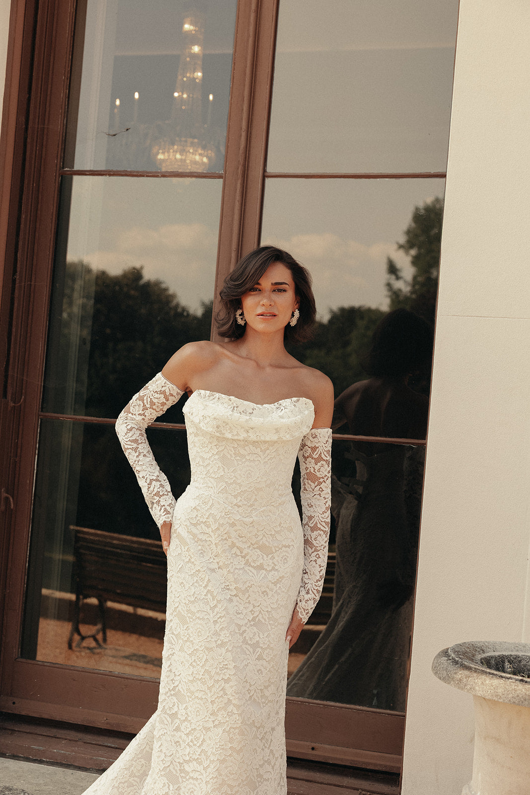 Woman in a ivory lace wedding dress standing in front of large windows with a scenic view.