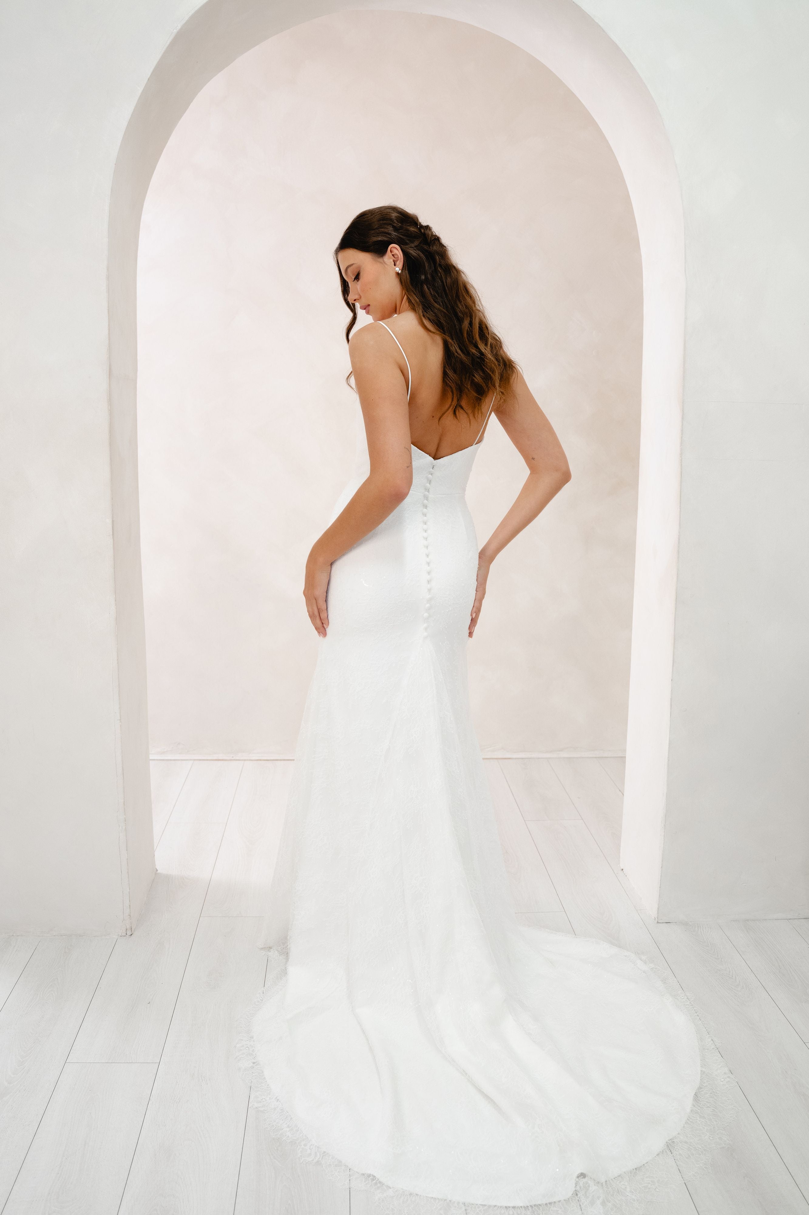 Woman in a white wedding dress standing in a bright, minimalistic room with an archway.