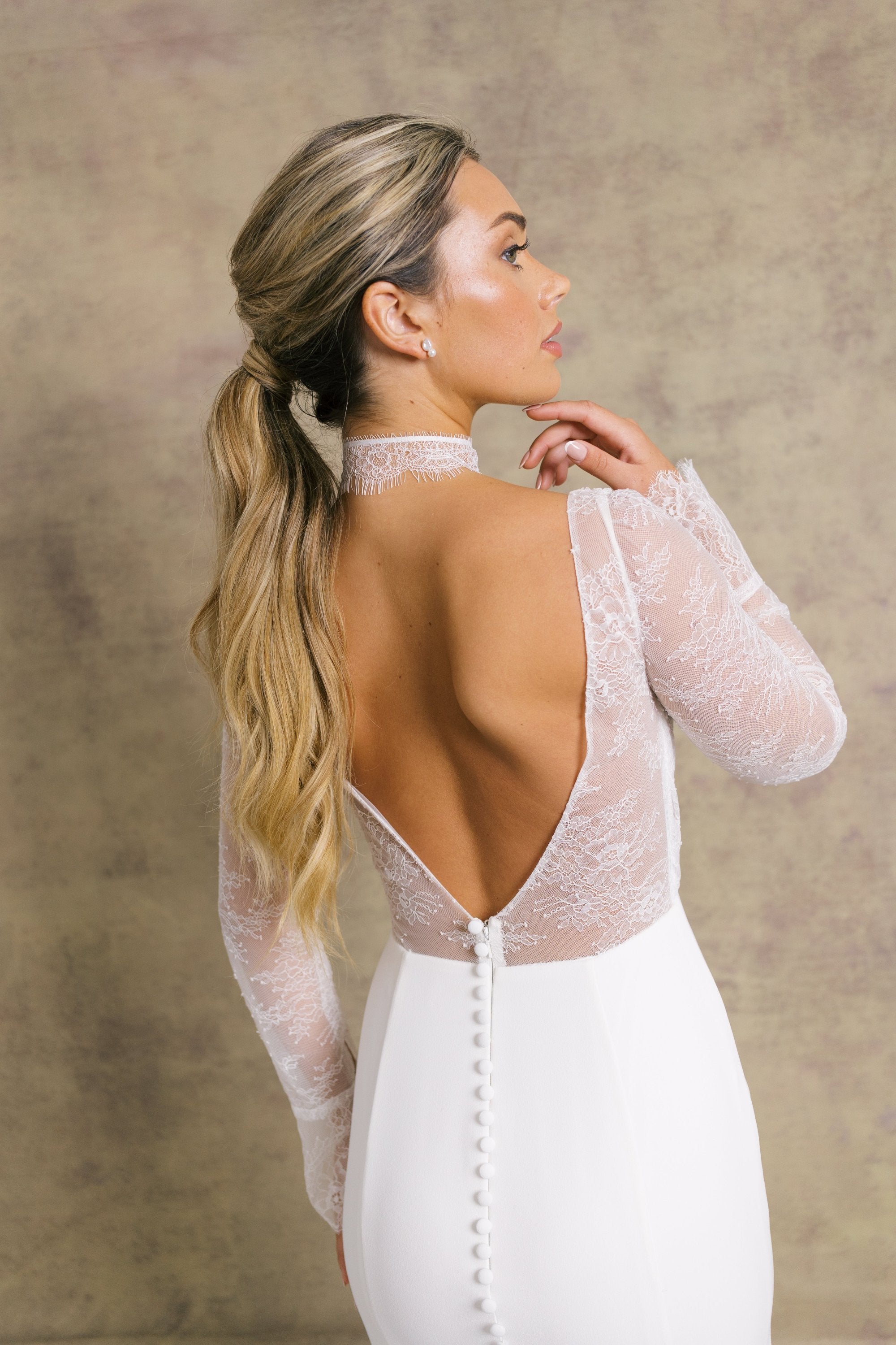 A woman in a pleated chantilly low back bodice wedding dress with long sleeves, finished with dreamy, flared cuffs, complemented on fitted crepe skirt.