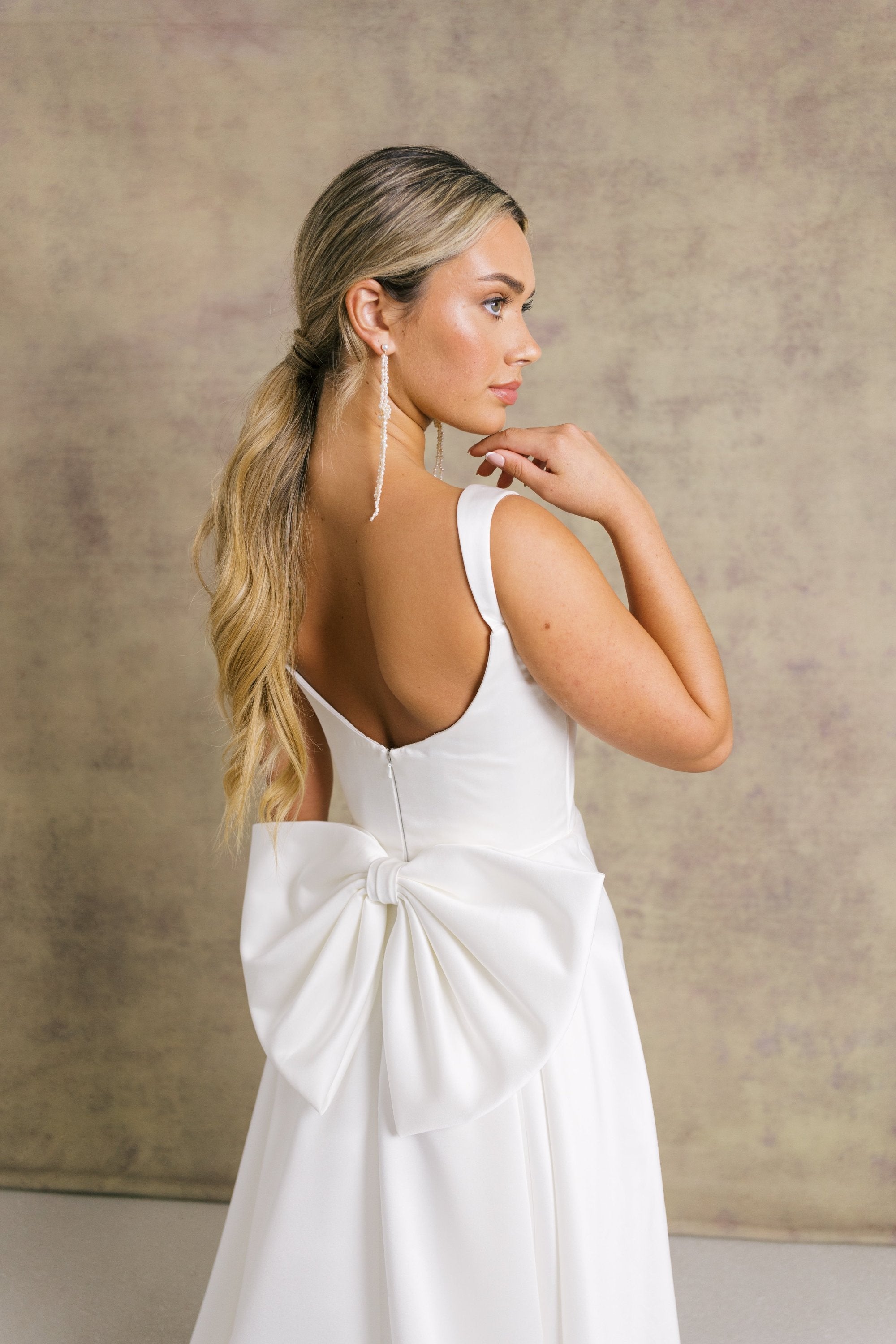 A woman in a satin striking low back wedding dress with a box pleated soft Aline skirt and bow.