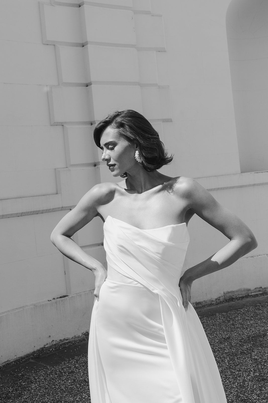 Woman in a strapless white dress standing against a light-colored wall.