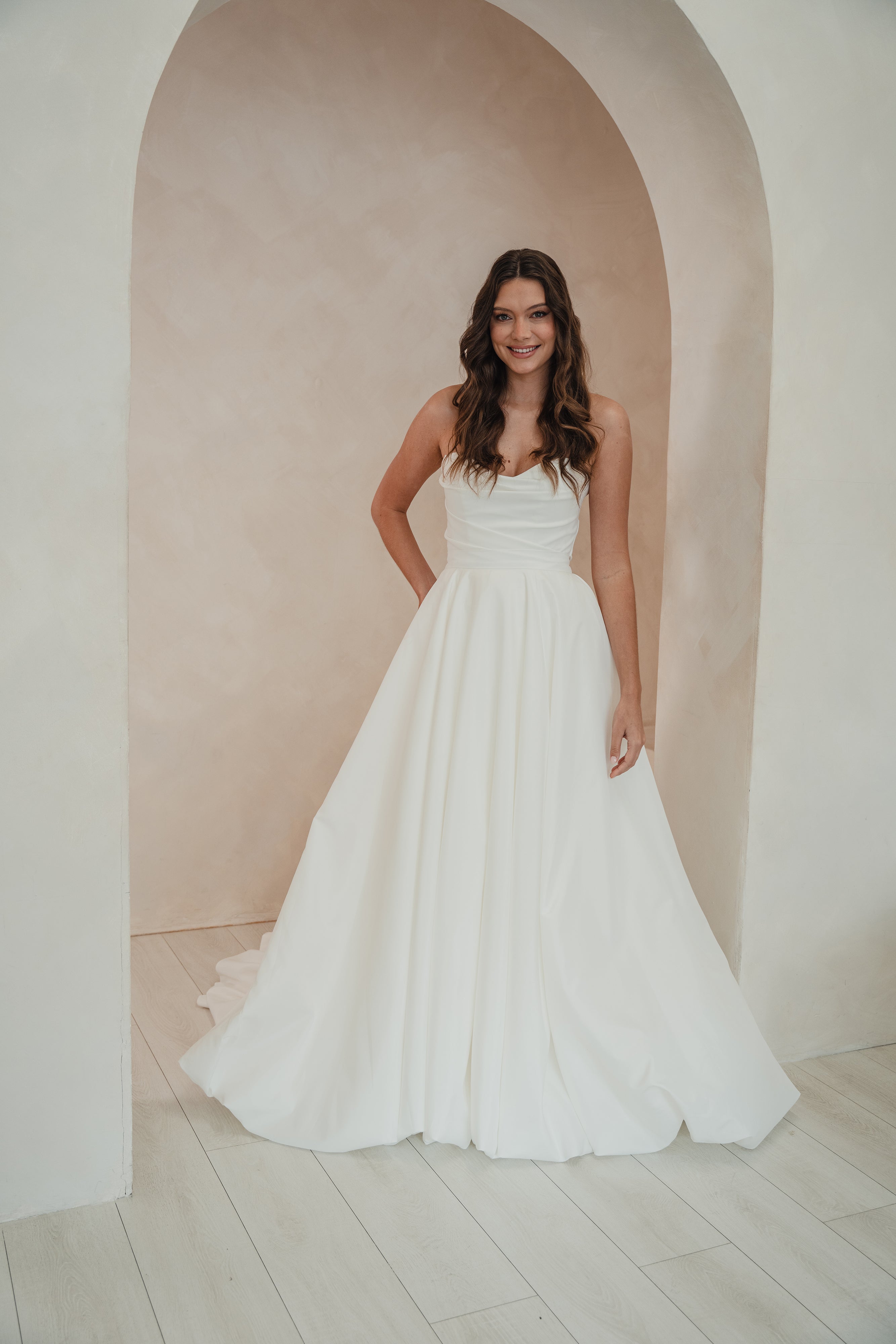 Woman in a white dress standing in a softly lit room with an archway.