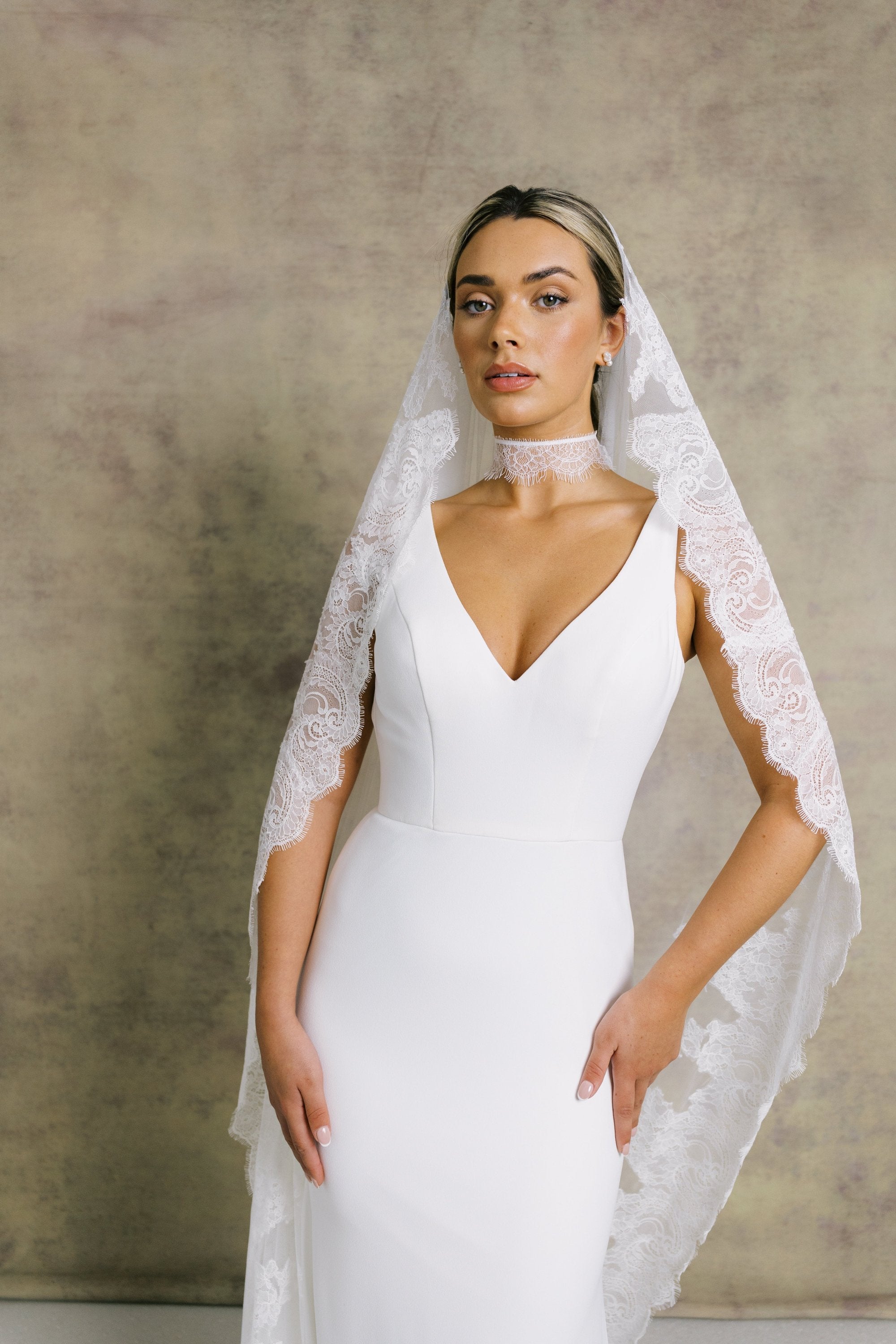 A woman in a sleek and elegant v neck fit and flare wedding dress, styled with Chantilly lace necktie and veil.