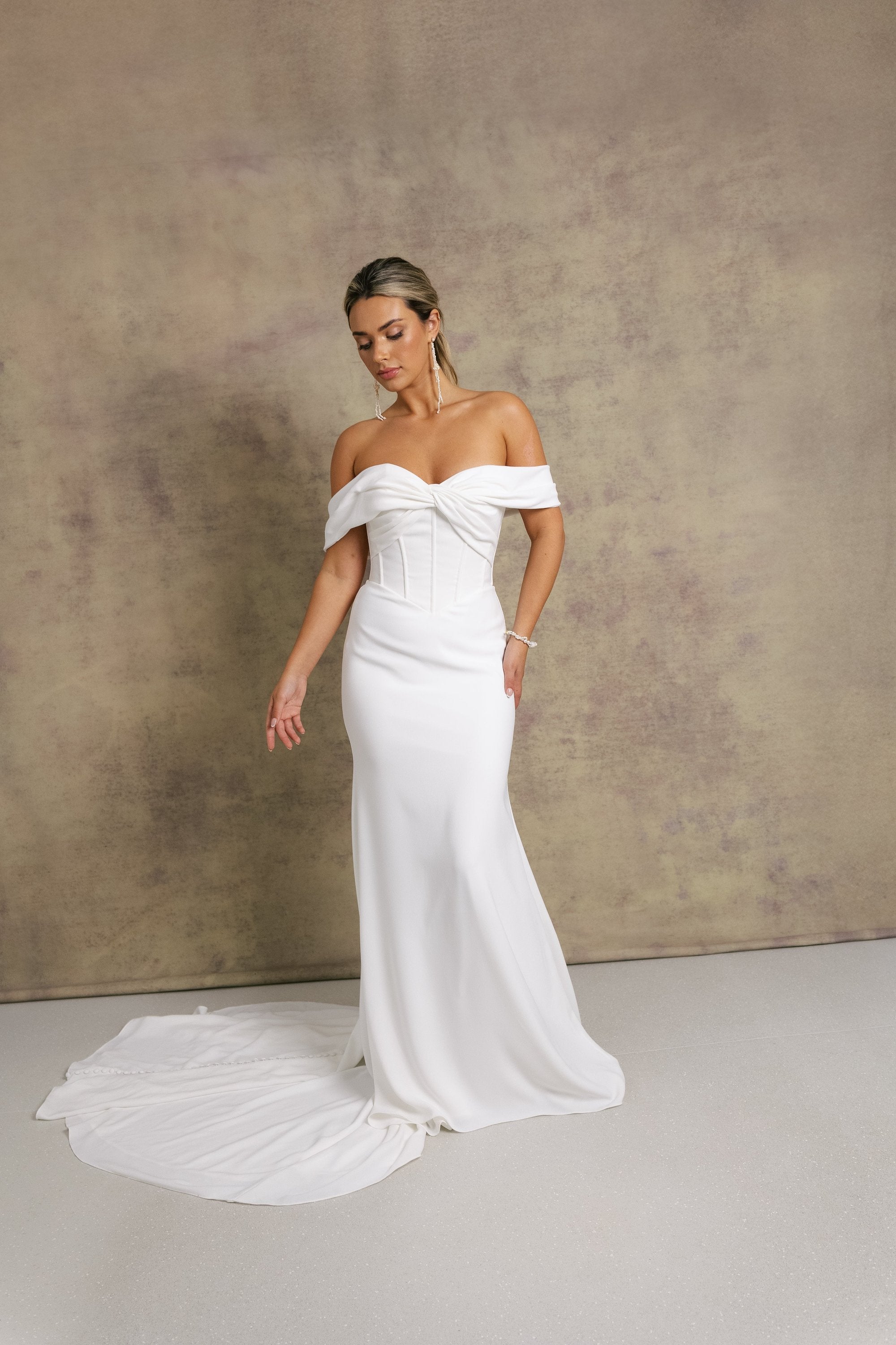 A woman in a gorgeous off shoulder sweetheart dropped waist wedding dress, featuring exposed boning on a crepe fit and flare skirt. 