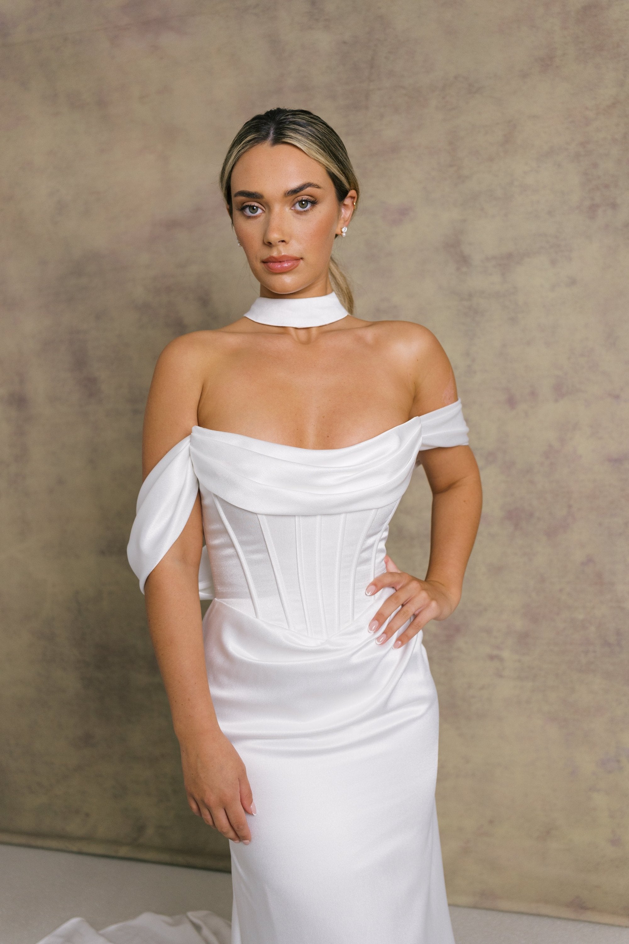 A woman in luxurious slipper satin wedding dress featuring a draped neckline on an exposed boned corset style drop waist bodice with draped bardot’s on our new ruched skirt.