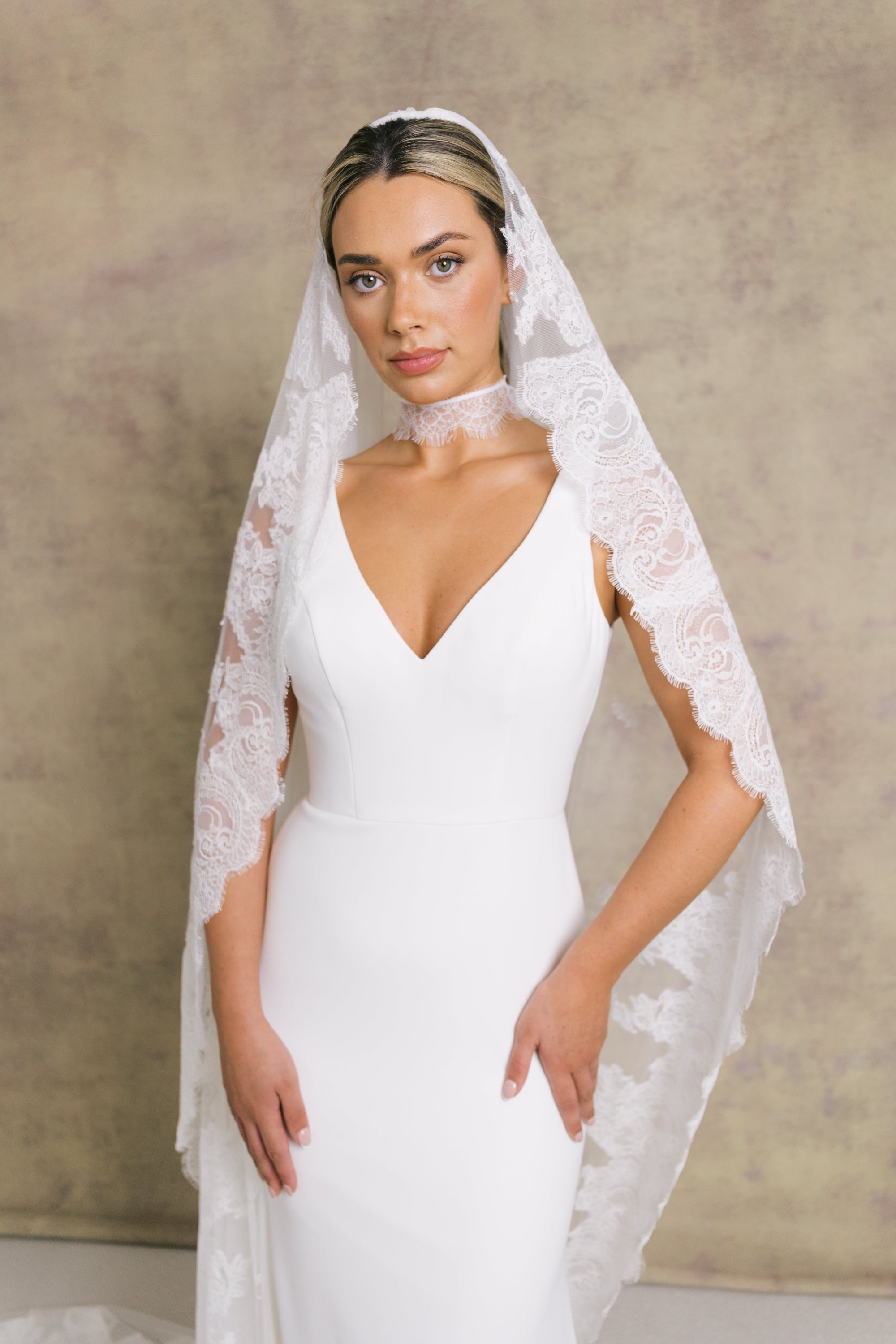 A women wearing a Chantilly lace wedding veil with eyelash edging, beautifully framing the face and dress.