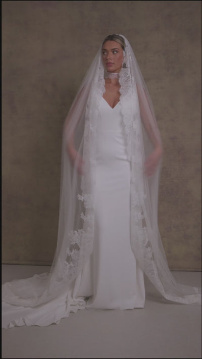 A woman in a sleek and elegant v neck fit and flare wedding dress, styled with Chantilly lace necktie and veil.