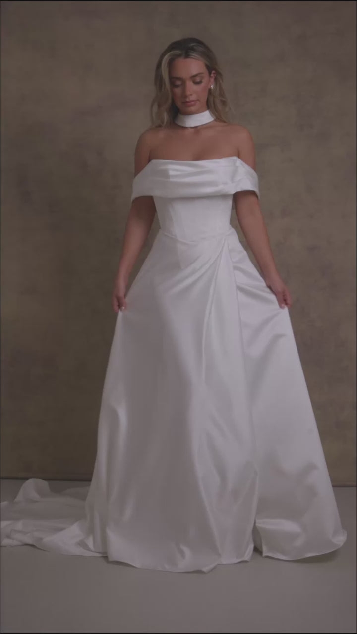  A woman in a subtle dropped waist wedding dress, off the shoulder boned bodice with a soft draped neckline and a wrap over leg split skirt in our gorgeous satin fabric.