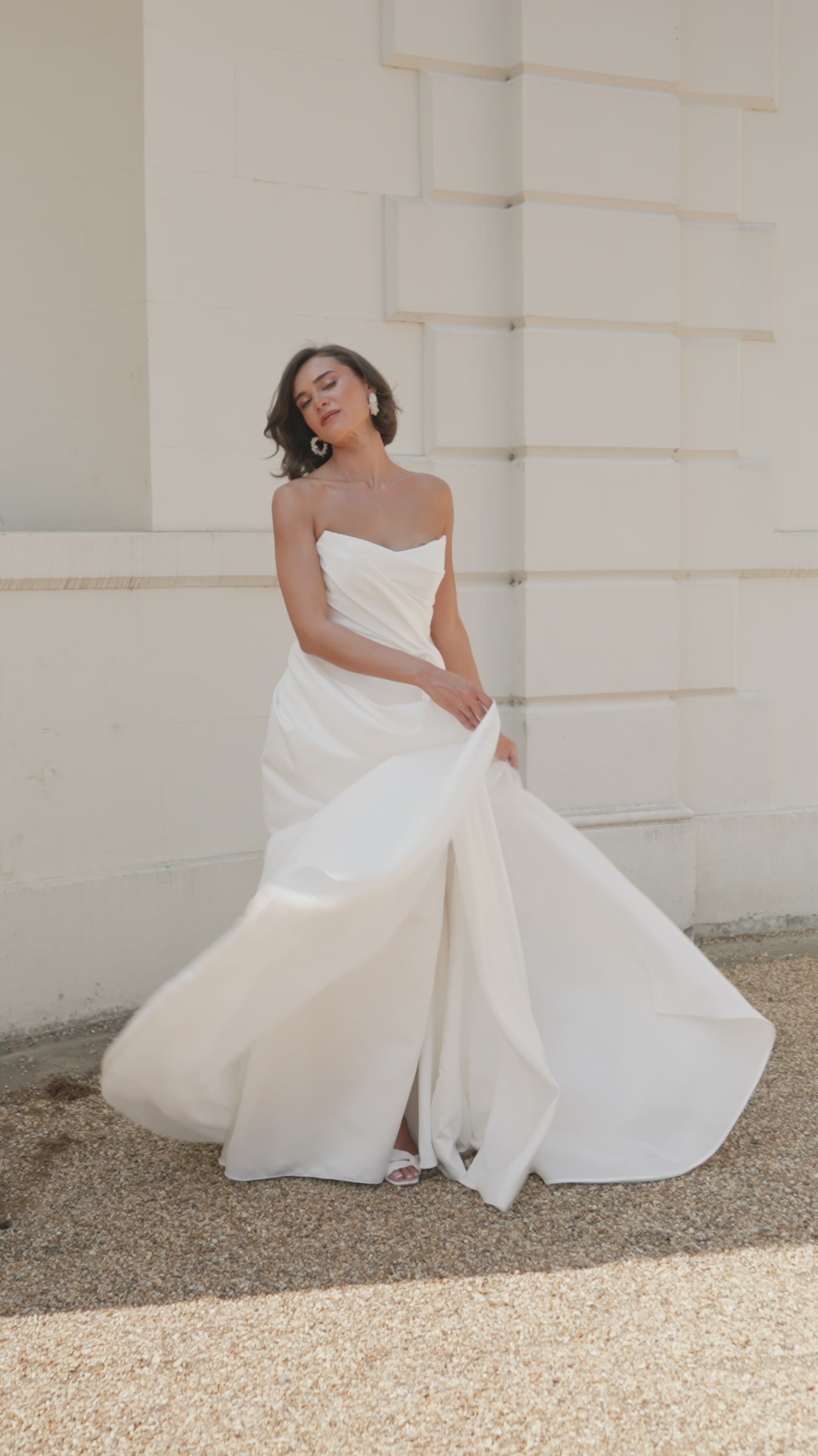 Woman in a strapless satin ivory wedding dress moving in an elegant architectural setting.