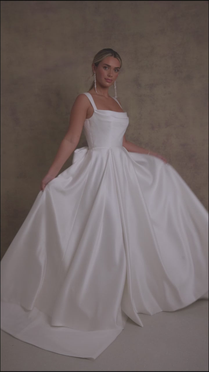 A woman in a satin striking cowl neckline wedding dress with a box pleated soft Aline skirt.