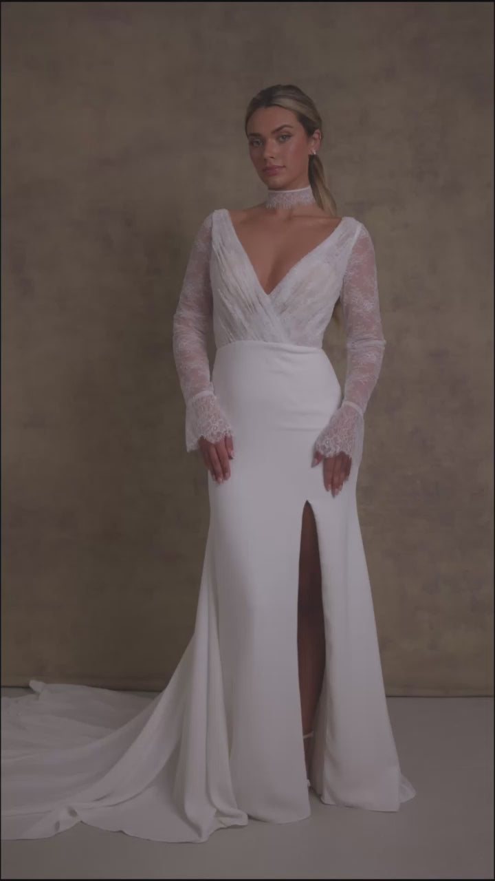 A woman in a pleated chantilly lace v neck bodice wedding dress with long sleeves, finished with dreamy, flared cuffs, complemented on fitted crepe skirt.