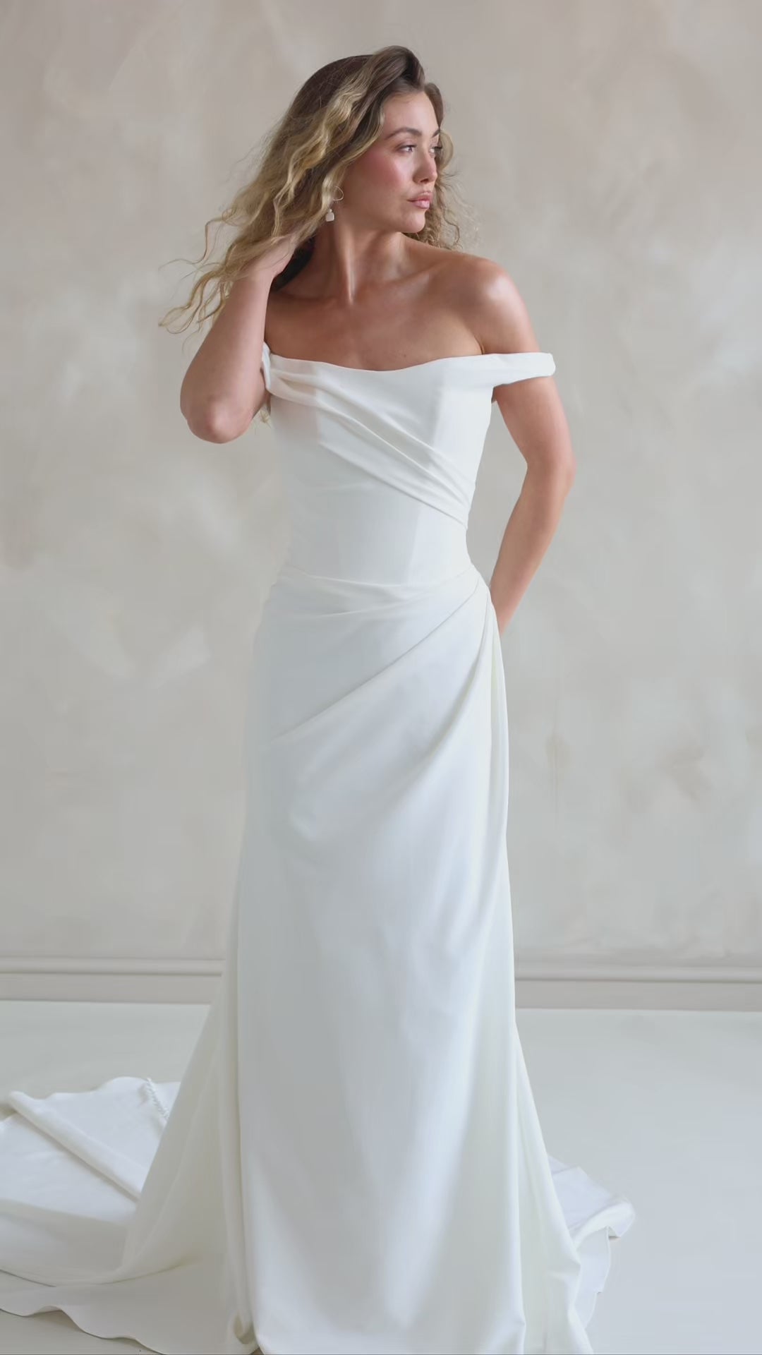 Bride wearing the Hadley off-the-shoulder stretch crepe wedding dress with draped neckline and button-back detail.