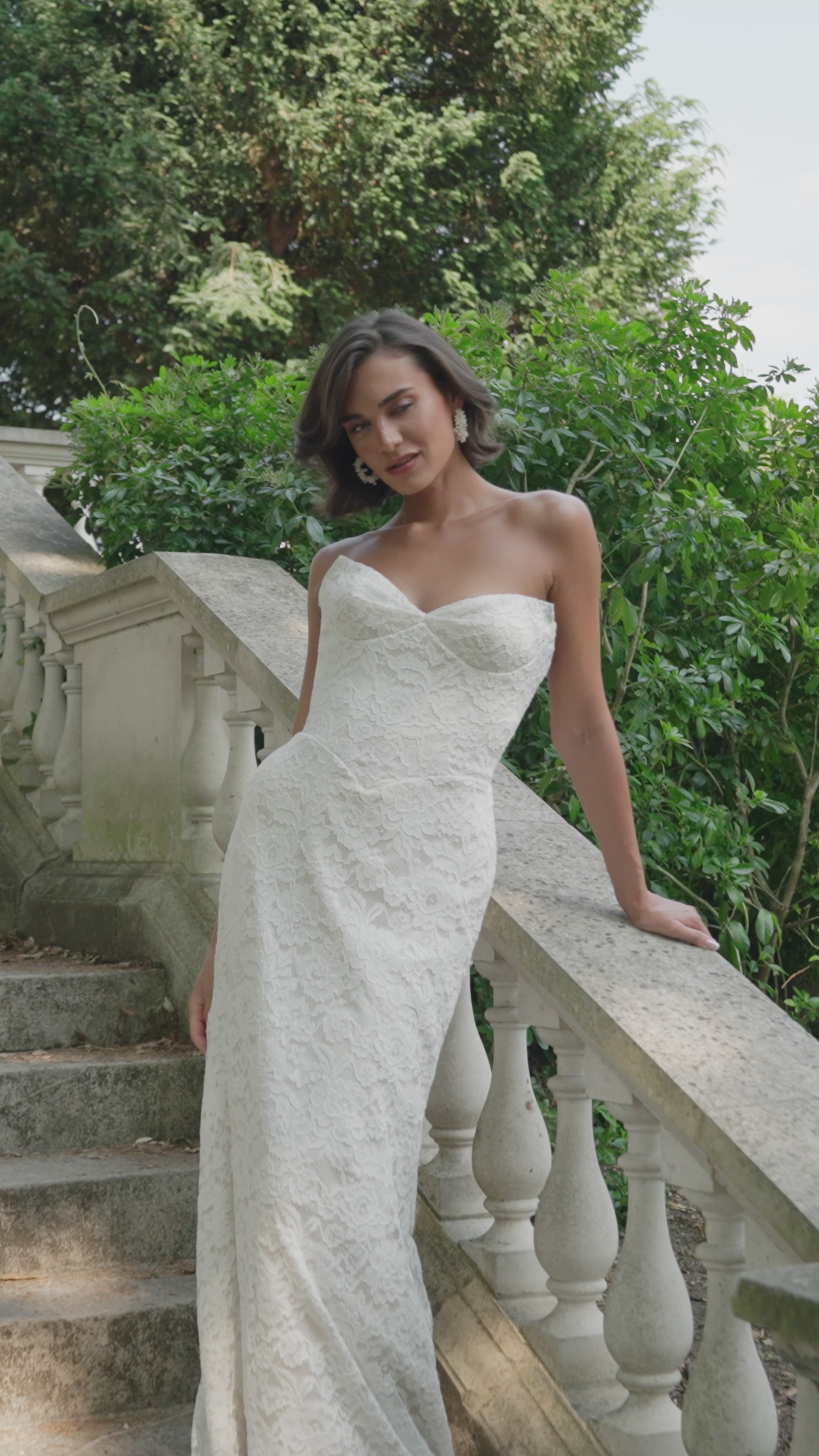 Woman in a ivory strapless dress moving on stone steps with greenery in the background
