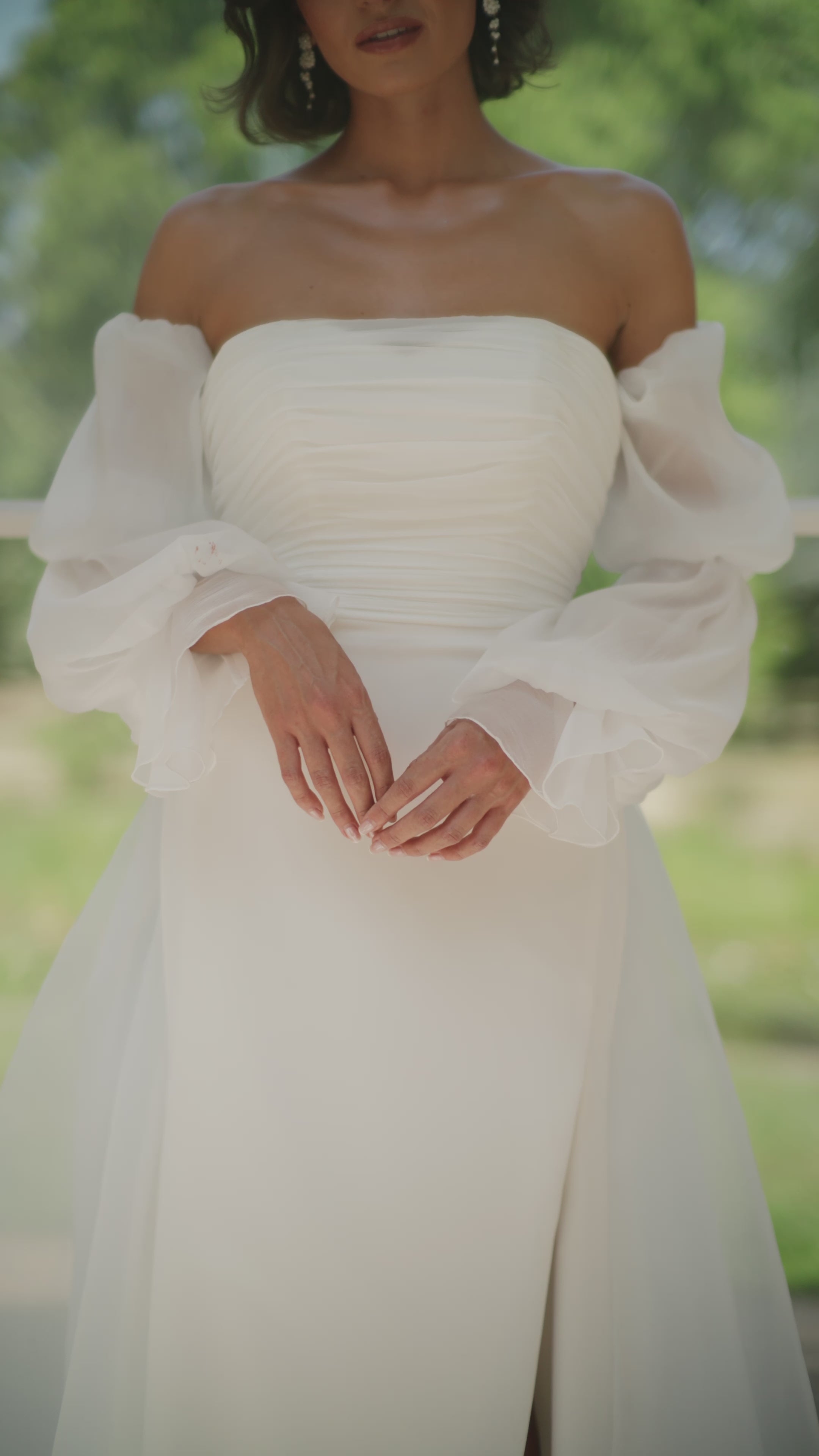 Woman in a ivory wedding dress standing in an outdoor setting with plants and a checkered floor.
