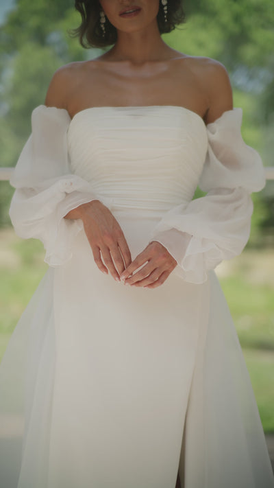 Woman in a ivory wedding dress standing in an outdoor setting with plants and a checkered floor.