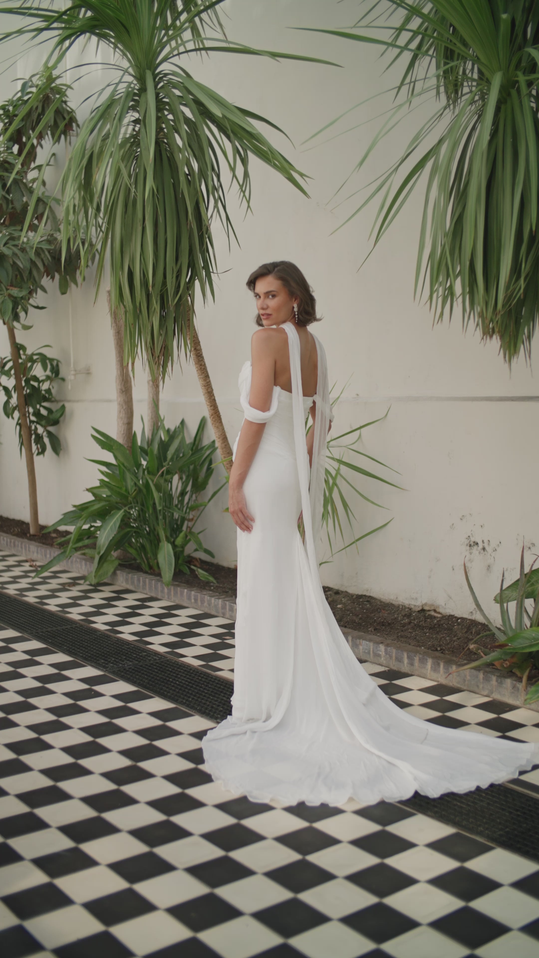 Woman in a ivory wedding dress moving in a tropical setting with plants and a checkered floor.