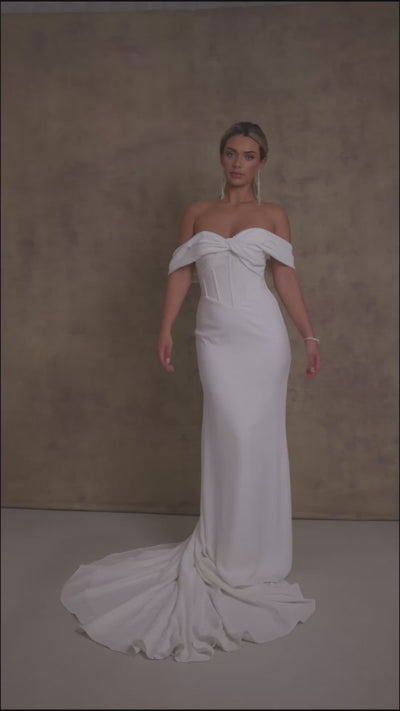 A woman in a gorgeous off shoulder sweetheart dropped waist wedding dress, featuring exposed boning on a crepe fit and flare skirt. 