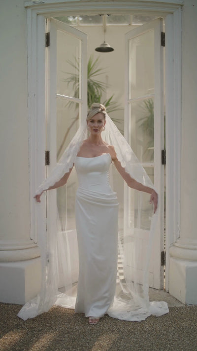 Woman in a ivory wedding dress and long lace wedding veil moving in front of a large glass door with columns.