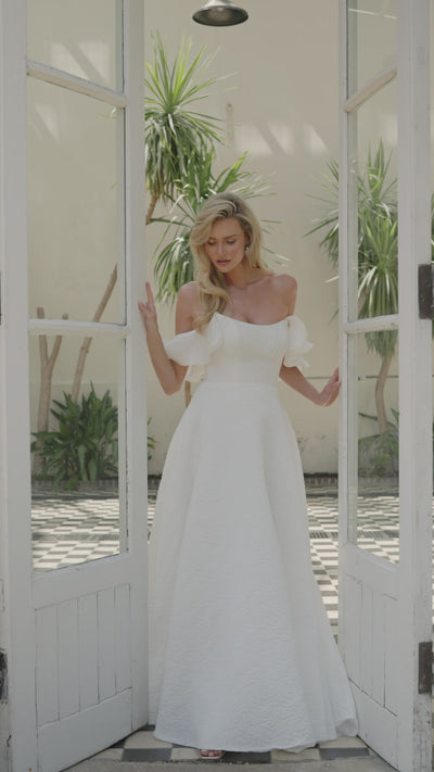 Woman in a ivory wedding dress moving in front of a glass door with palm trees in the background