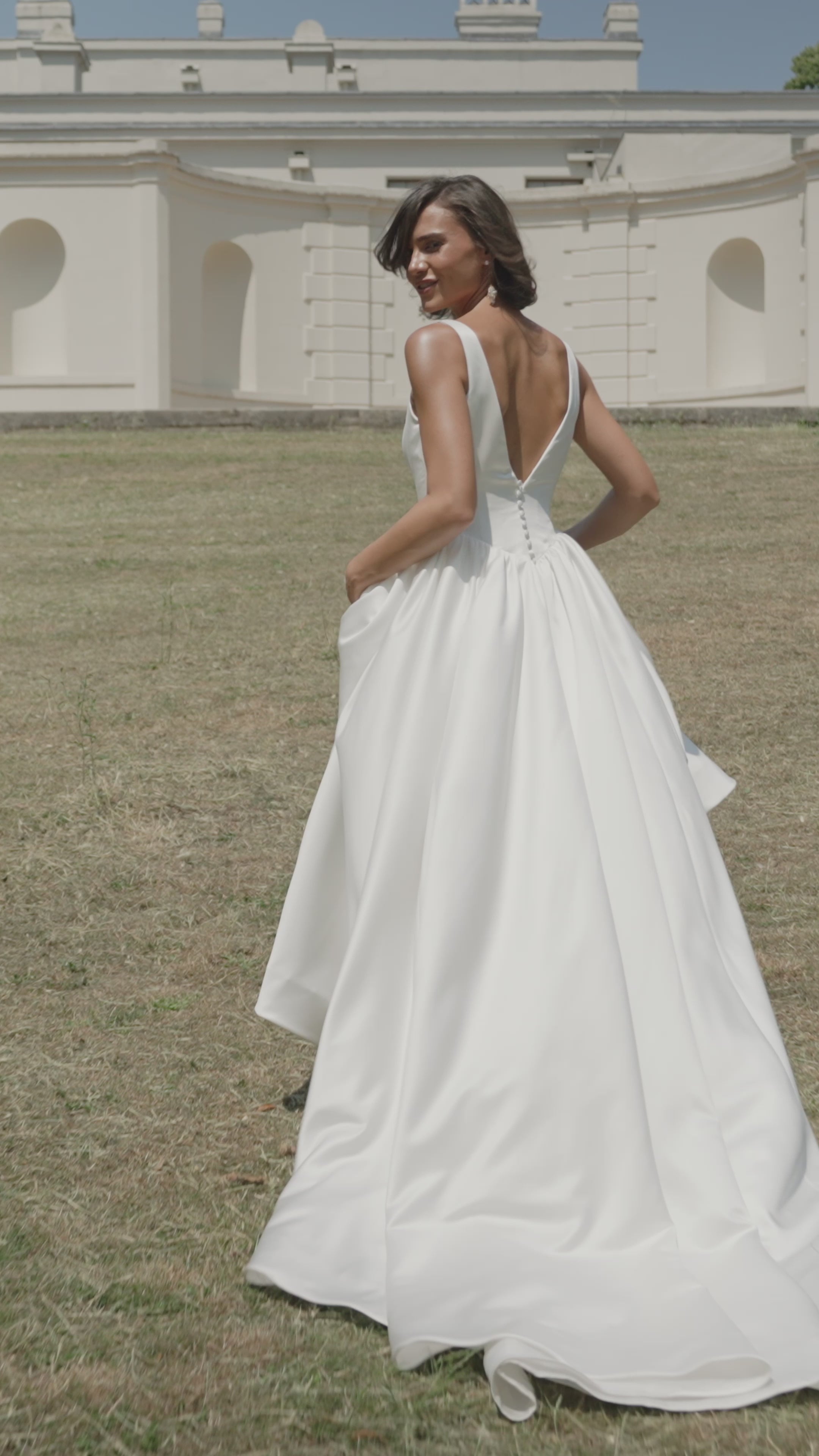 Woman in a ivory satin wedding dress moving on grass with a building in the background
