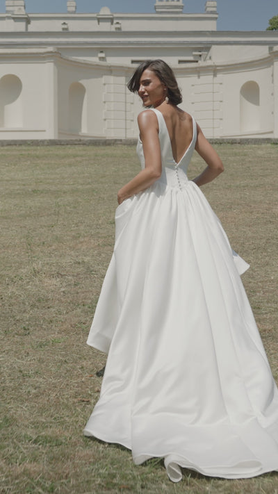 Woman in a ivory satin wedding dress moving on grass with a building in the background