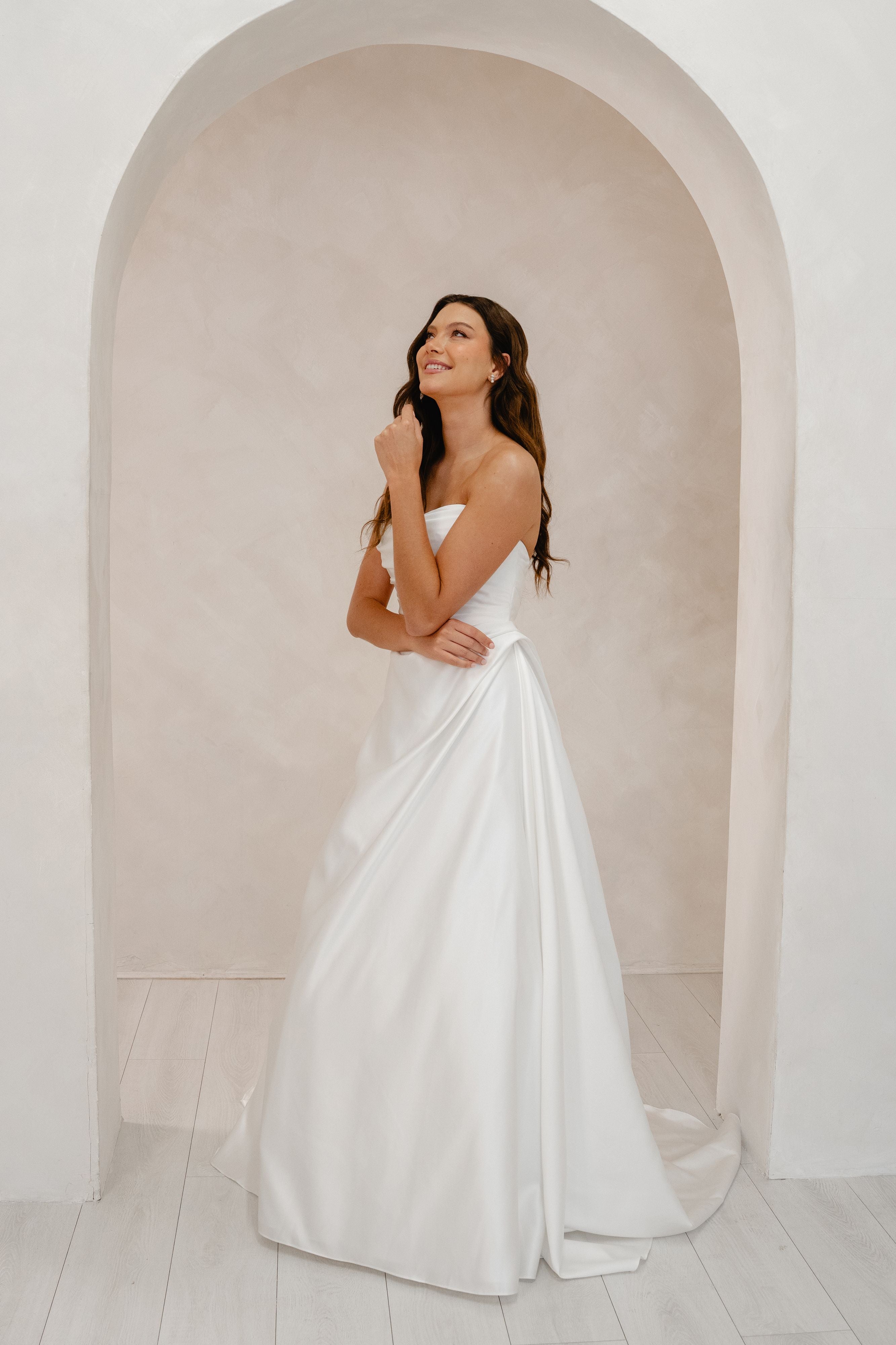 Woman in a white strapless gown standing in a room with an archway.
