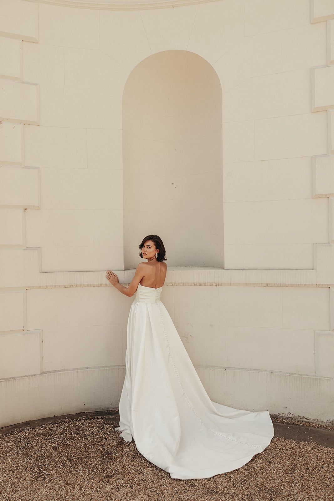 Woman in a ivory satin wedding dress standing against a beige wall.
