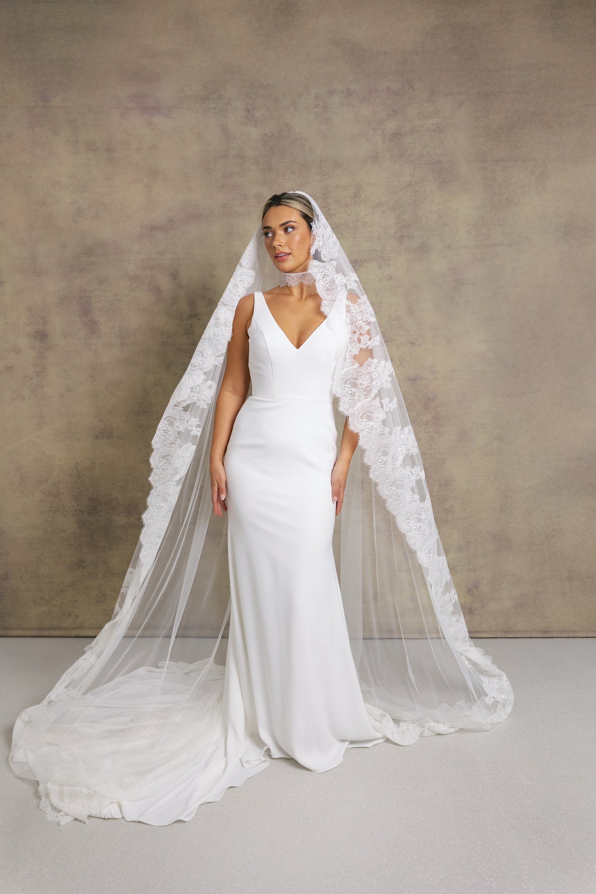 A woman in a sleek and elegant v neck fit and flare wedding dress, styled with Chantilly lace necktie and veil.