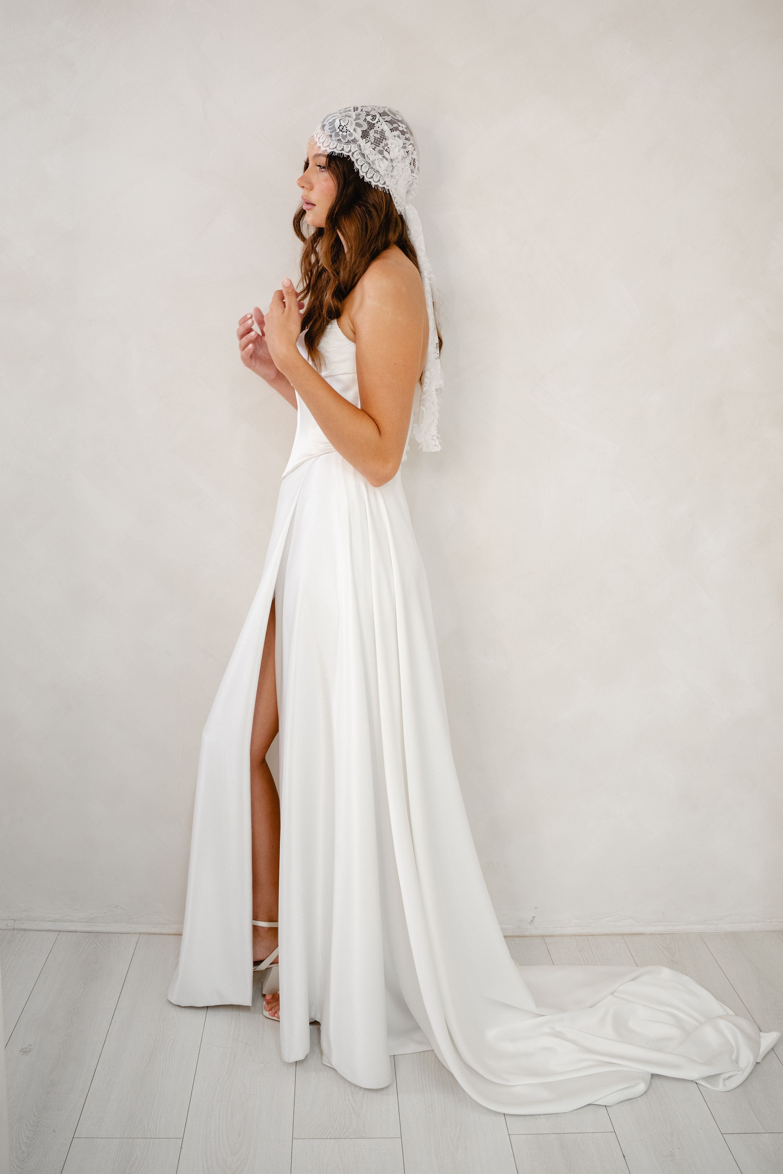 Woman in a white wedding dress with a head covering against a plain background