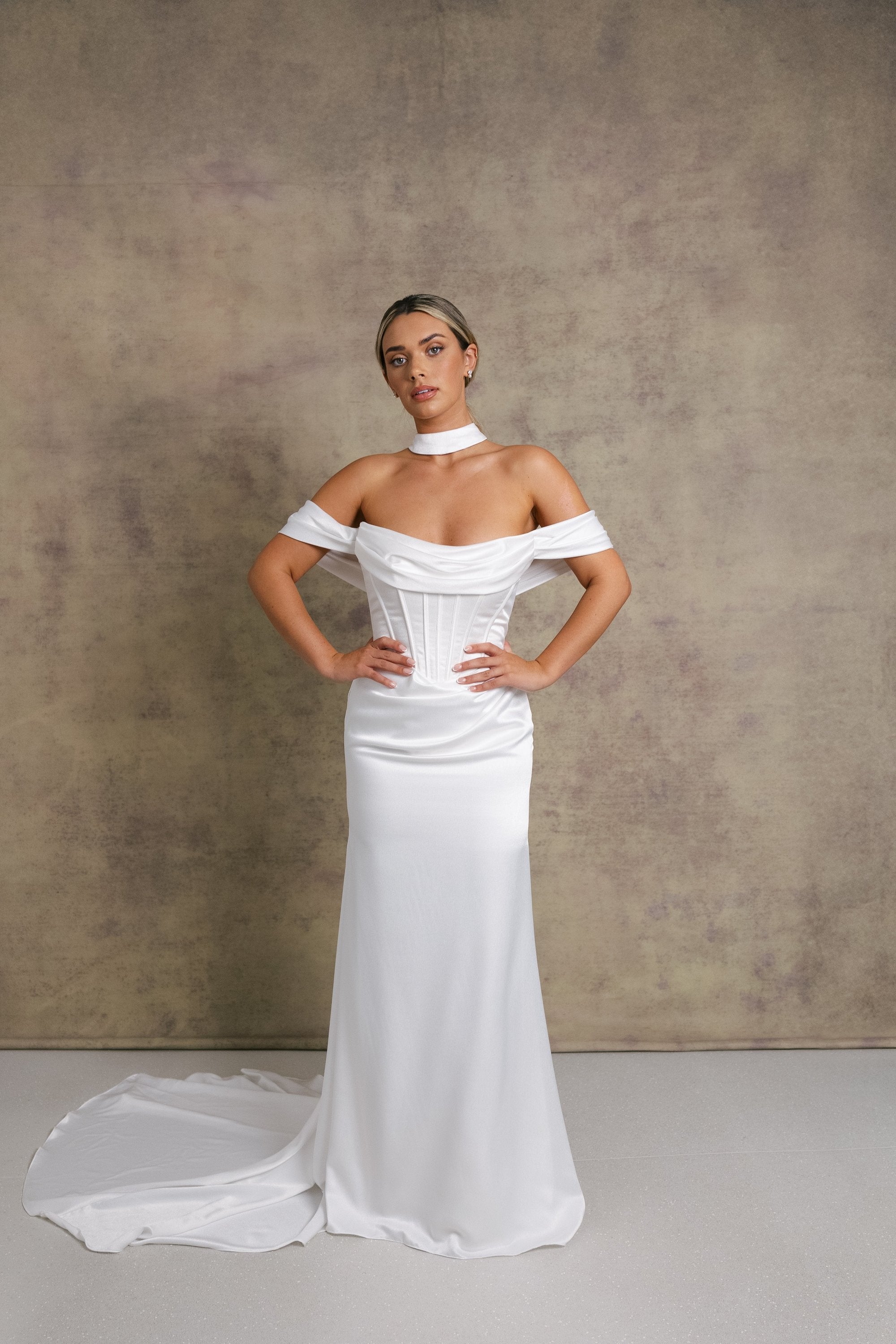 A woman in luxurious slipper satin wedding dress featuring a draped neckline on an exposed boned corset style drop waist bodice with draped bardot’s on our new ruched skirt.