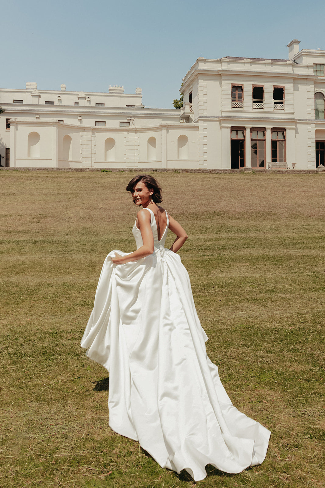 Woman in a ivory wedding dress standing on grass with a large building in the background