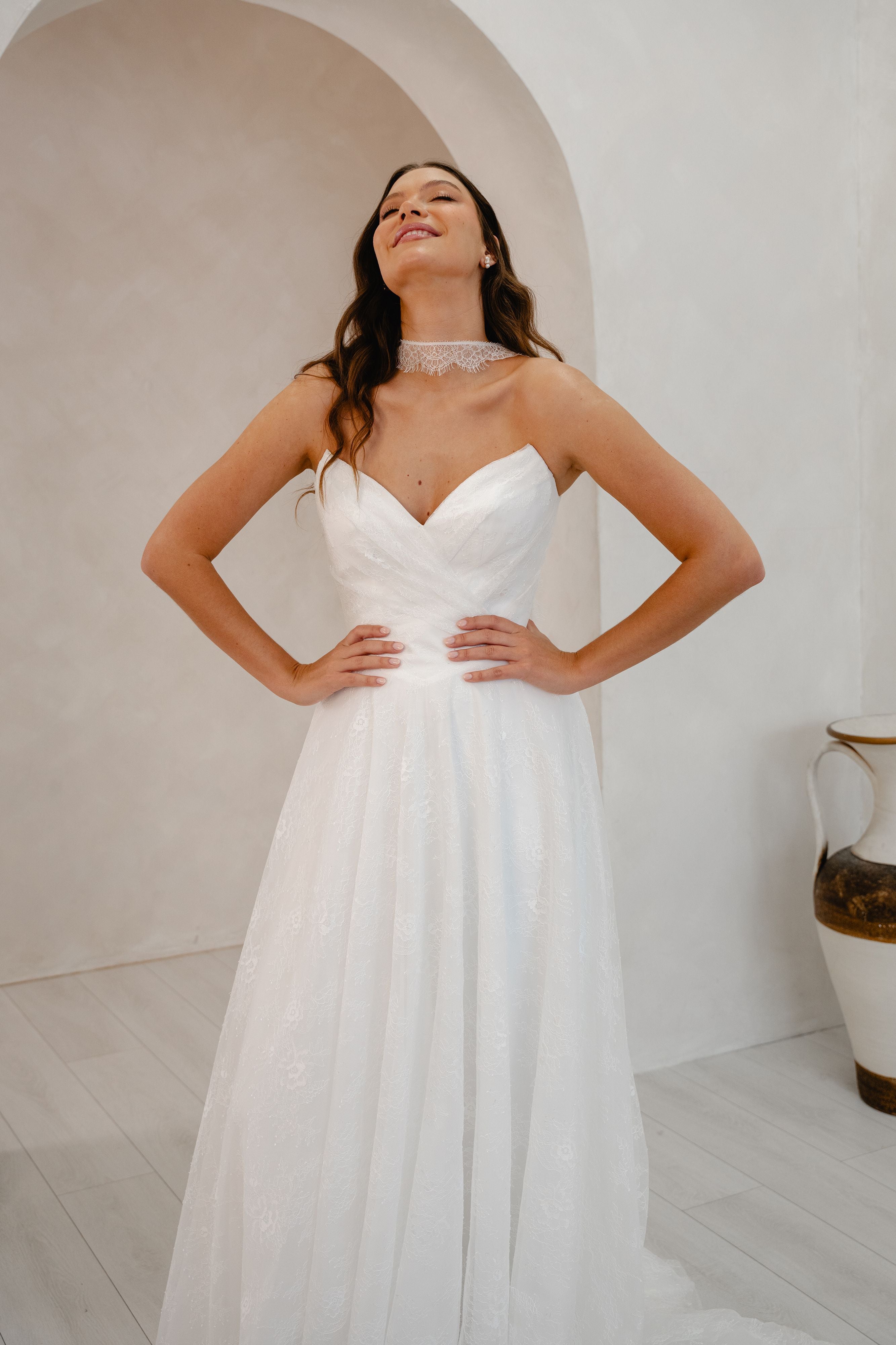 Woman wearing a white wedding dress in a minimalistic room with a vase in the background.