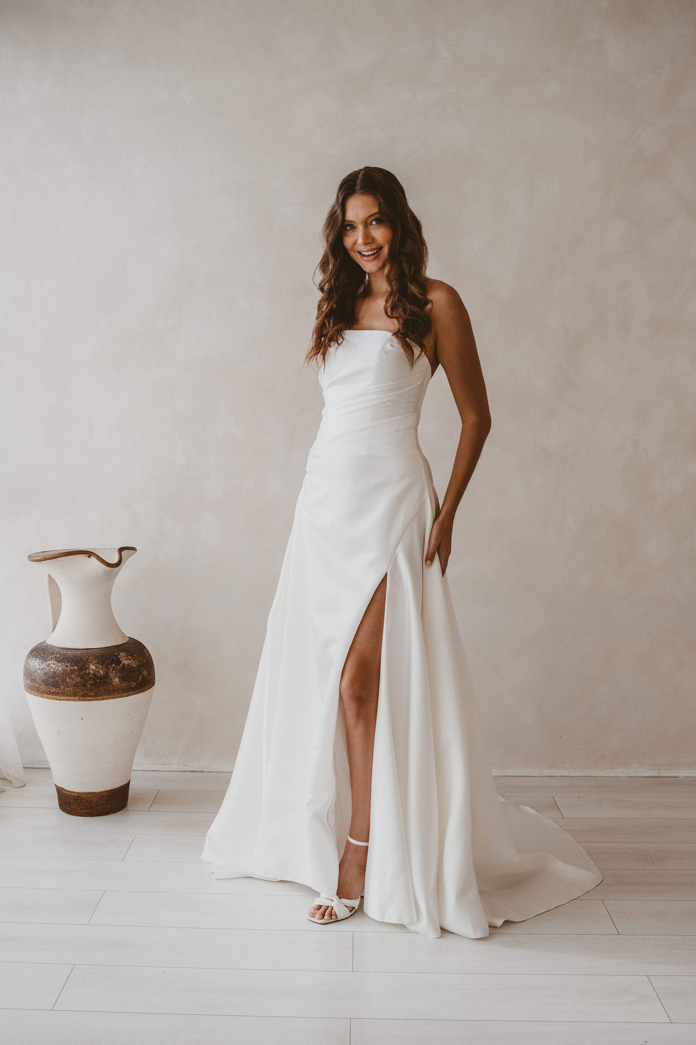 Woman in a white strapless gown with a high slit standing in a minimalistic room.