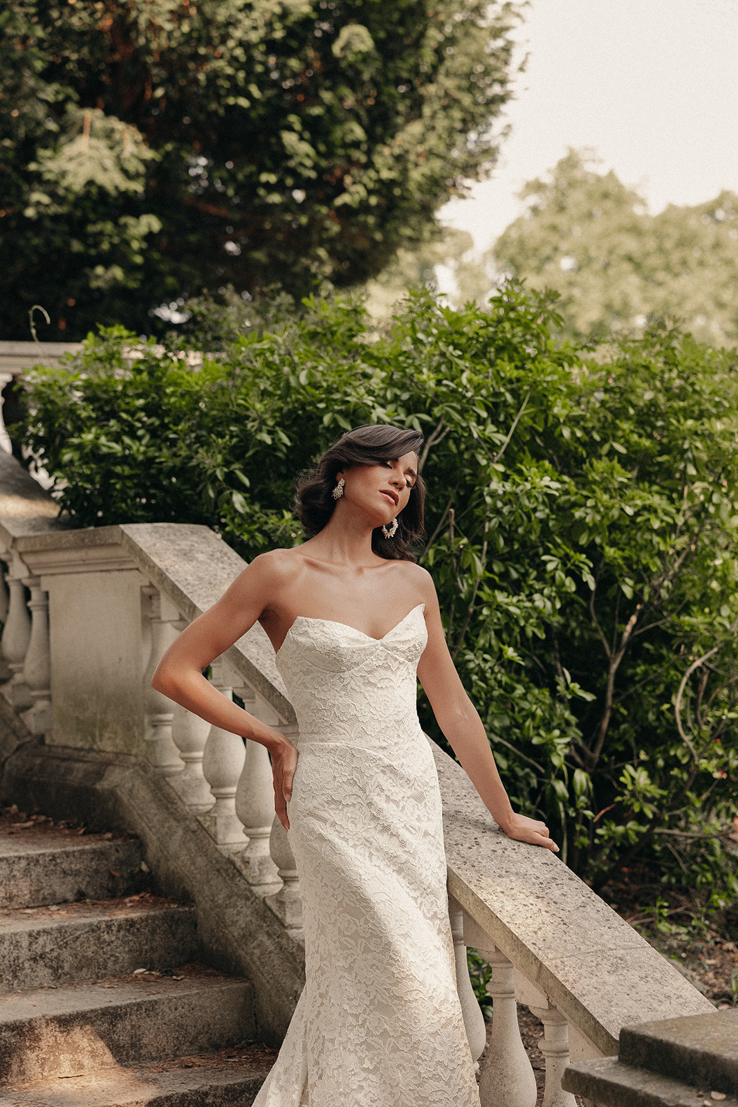 Woman in a ivory strapless dress standing on stone steps with greenery in the background