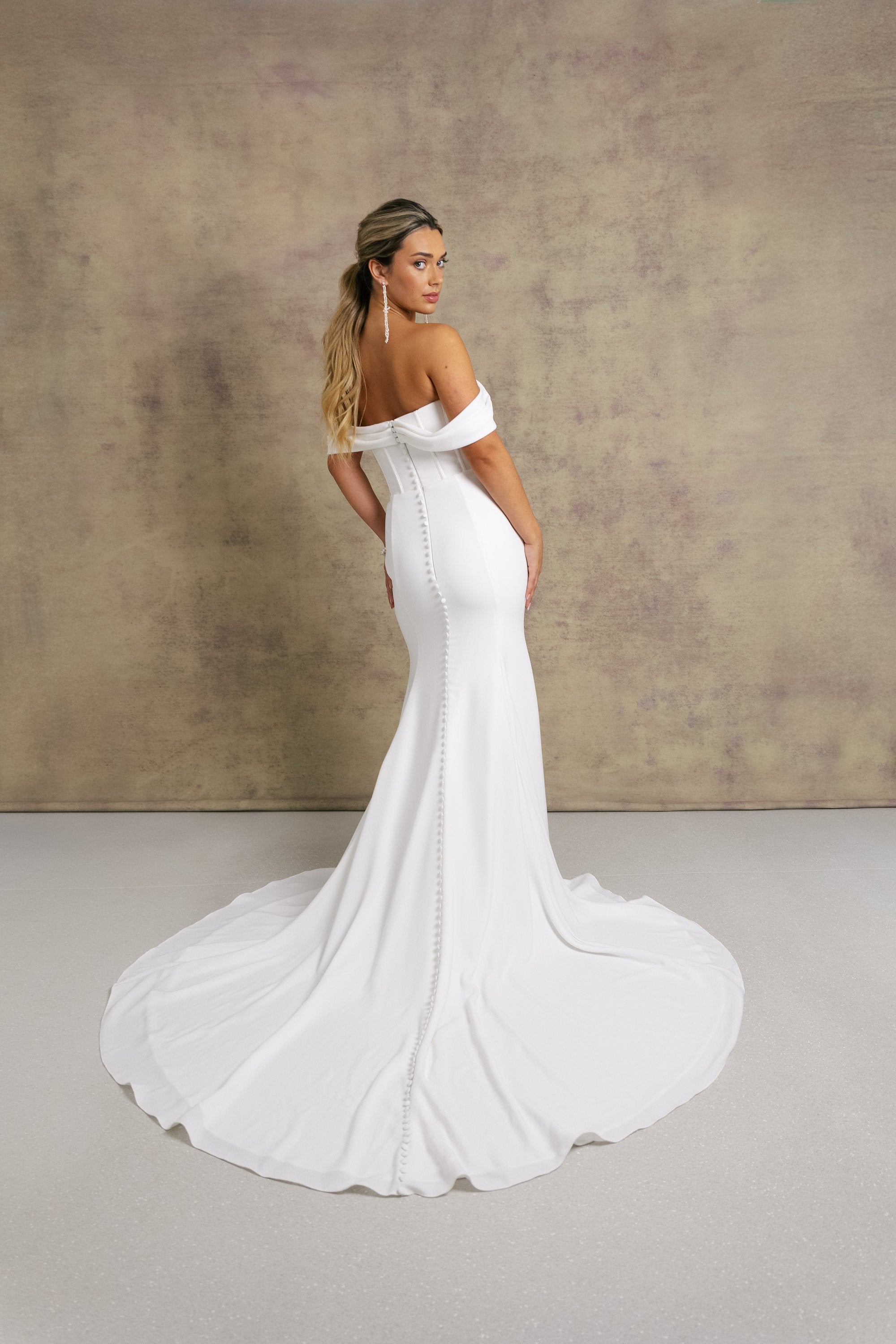 A woman in a gorgeous off shoulder sweetheart dropped waist wedding dress, featuring exposed boning on a crepe fit and flare skirt. 