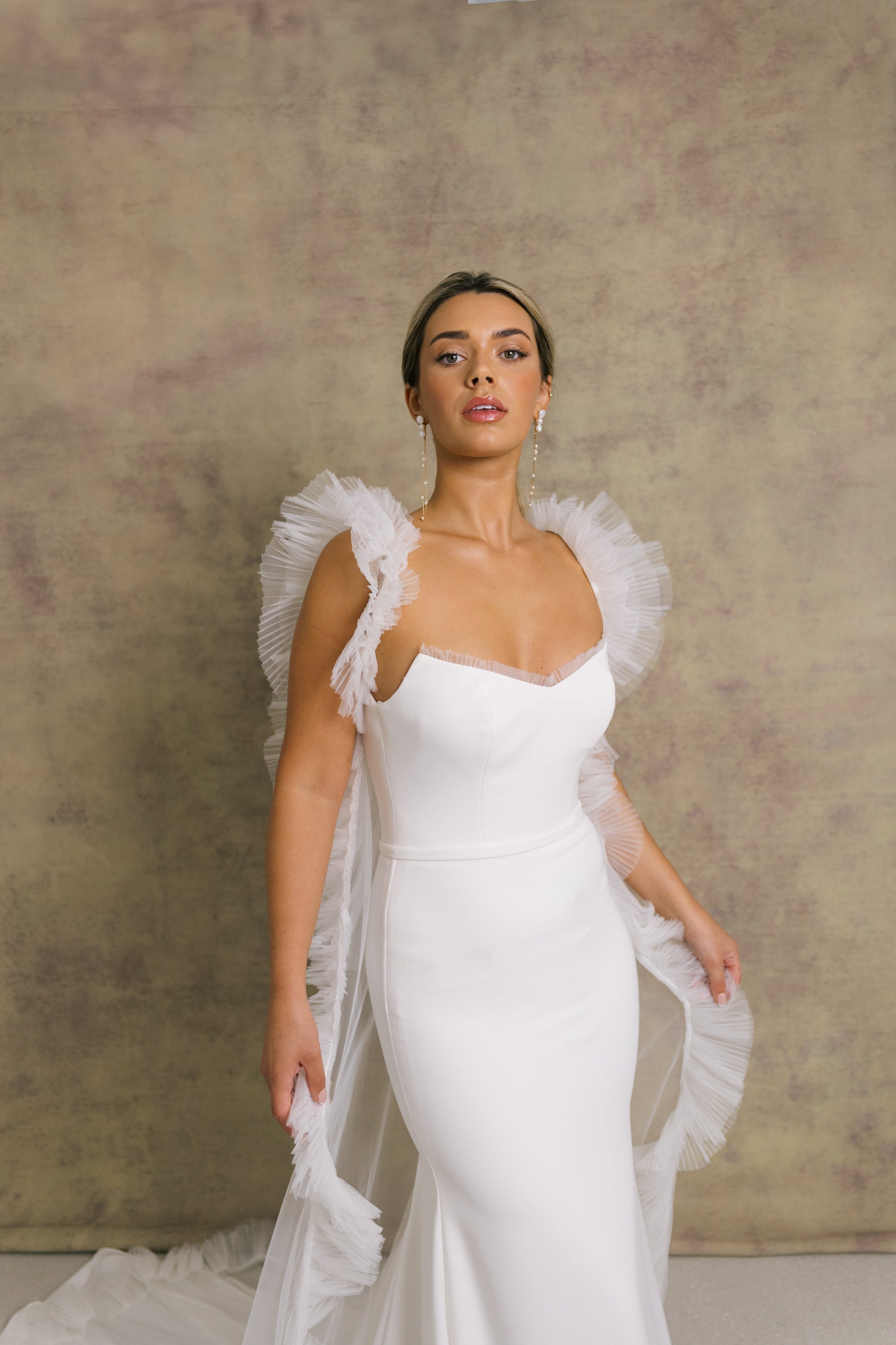 A woman in a strapless ivory wedding gown with a sweetheart neckline and tulle wedding cape