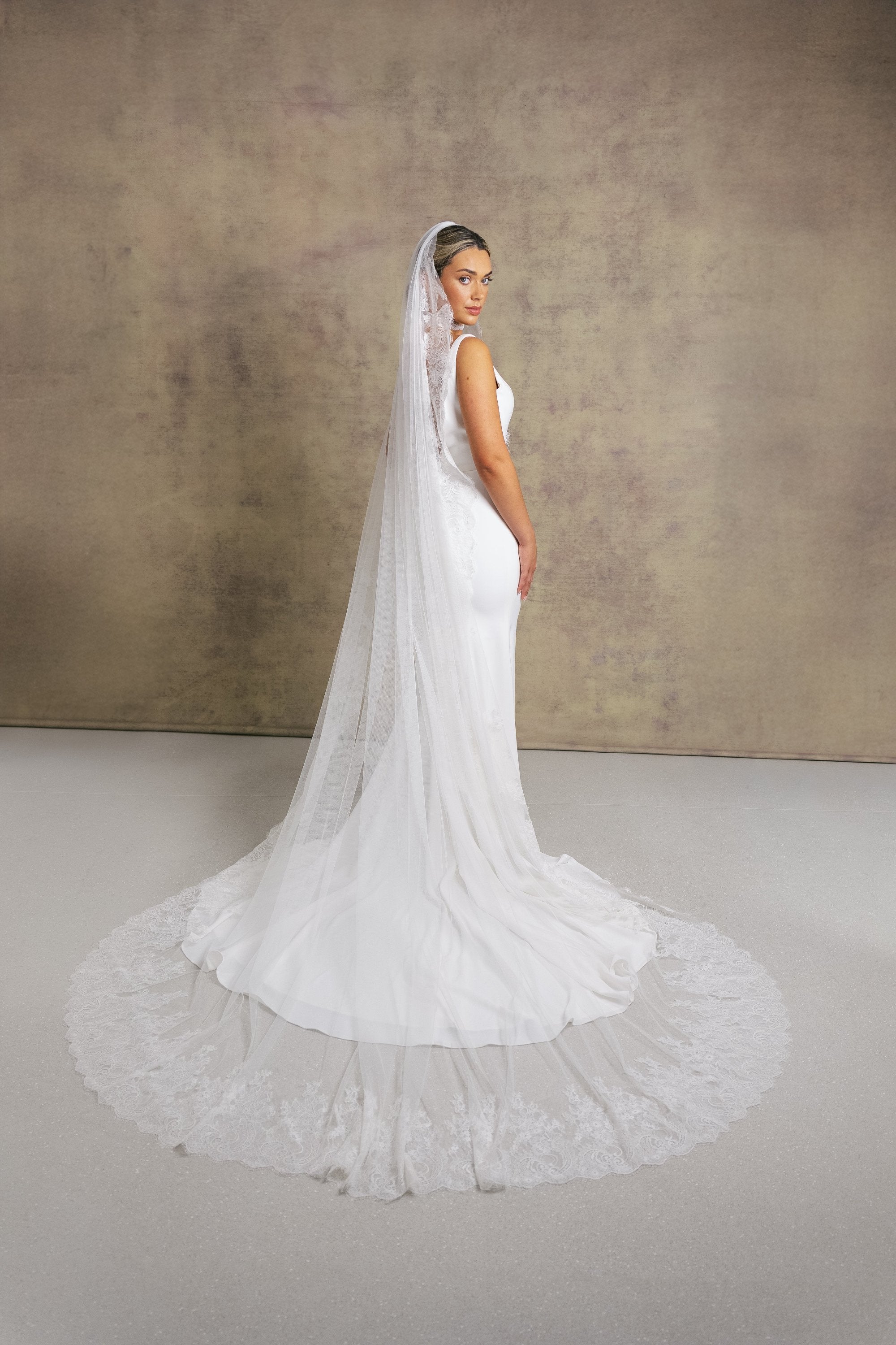 A woman in a sleek and elegant v neck fit and flare wedding dress, styled with Chantilly lace necktie and veil.