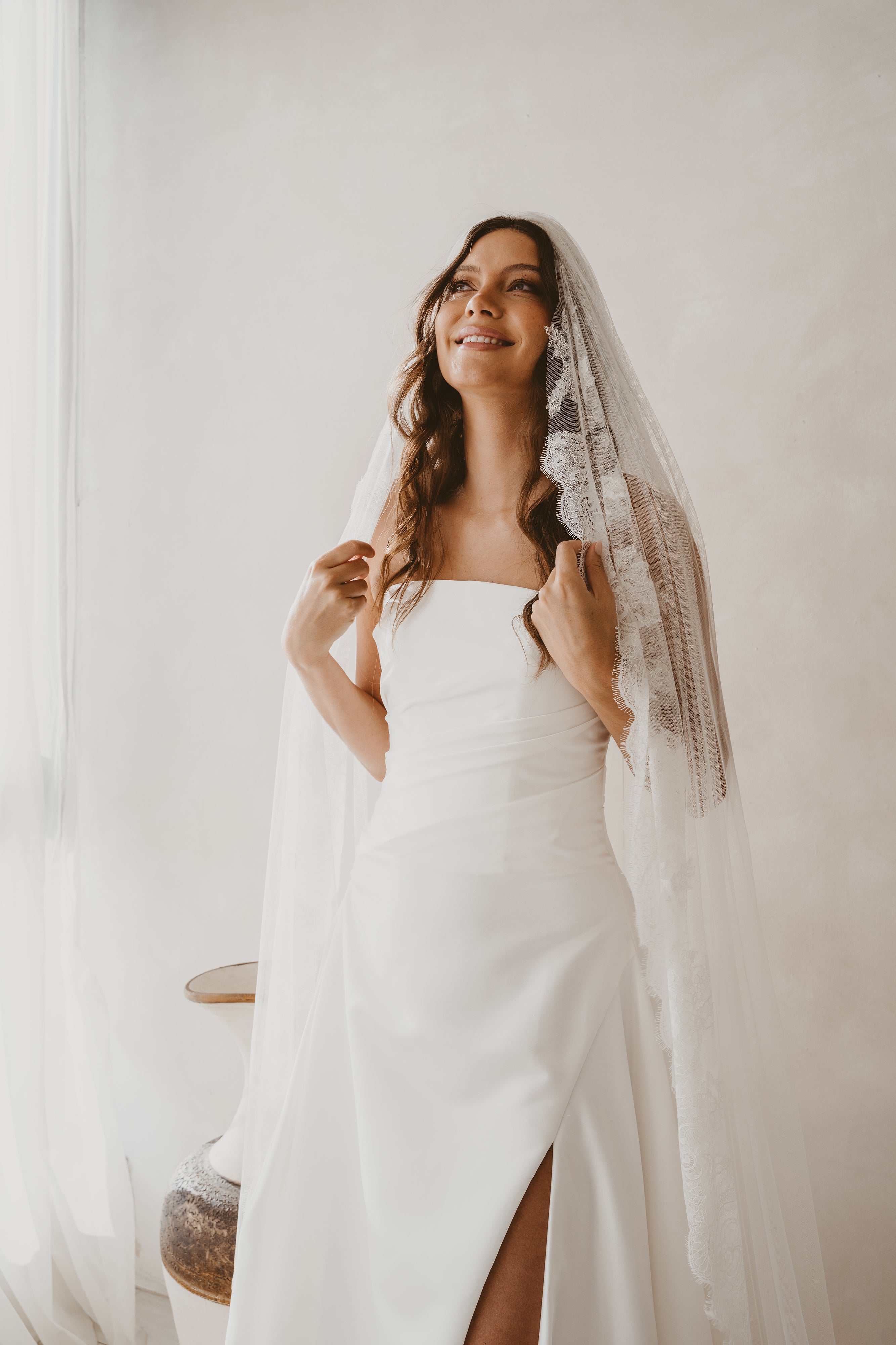 Woman in a white wedding dress with a veil against a plain background
