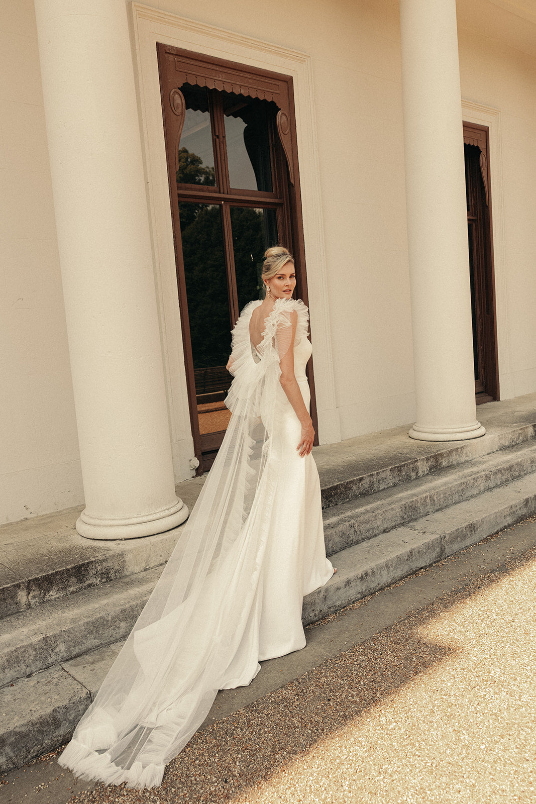 Woman in a ivory wedding dress standing on steps of a classical building.