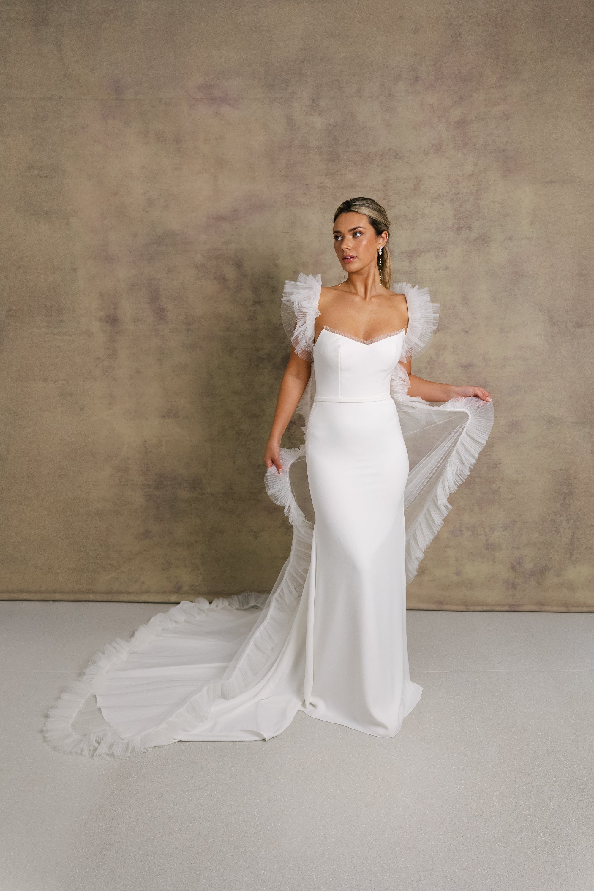 A woman in a strapless ivory wedding gown with a sweetheart neckline and tulle wedding cape covering your shoulders